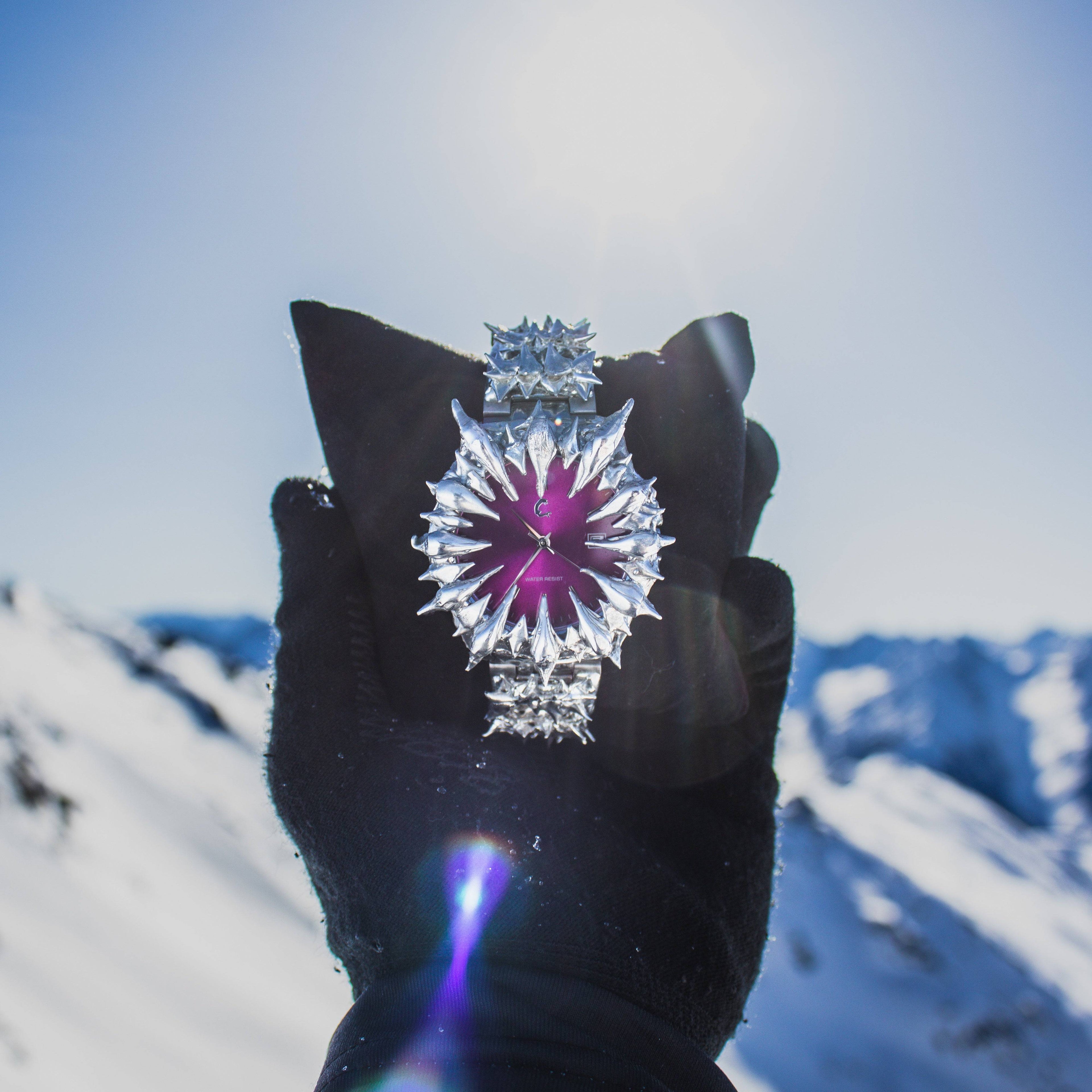 AMETHYST THORN spiked wristwatch held against snowy mountain backdrop, showcasing its vibrant purple dial and metallic spikes.