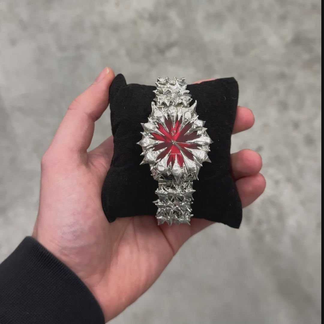 Ruby Thorn chrome watch with spiked design and red dial displayed on a black cushion, highlighting its bold jewelry aesthetic.