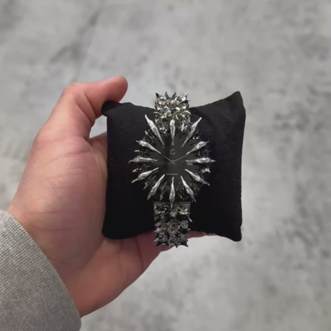 Hand holding the MIDNIGHT THORN spiked watch on a black cushion, showcasing its chrome spikes and resilient quartz build in a lifestyle setting.