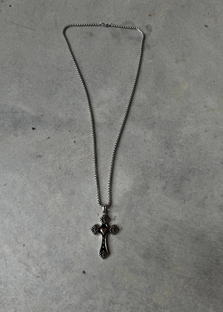 Full view of Bloom Cross Necklace showcasing its elegant floral steel cross pendant and durable chain on a concrete background.